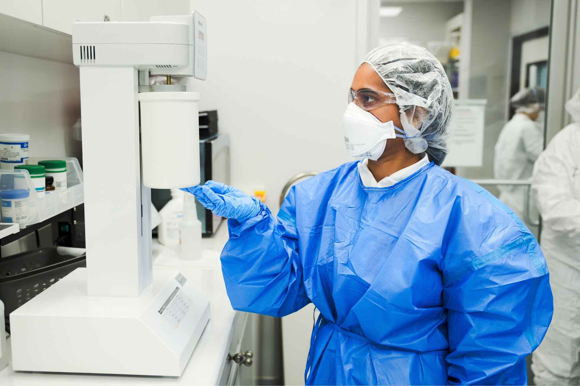 Pharmacist in protective gear dispensing medication in a compounding pharmacy.