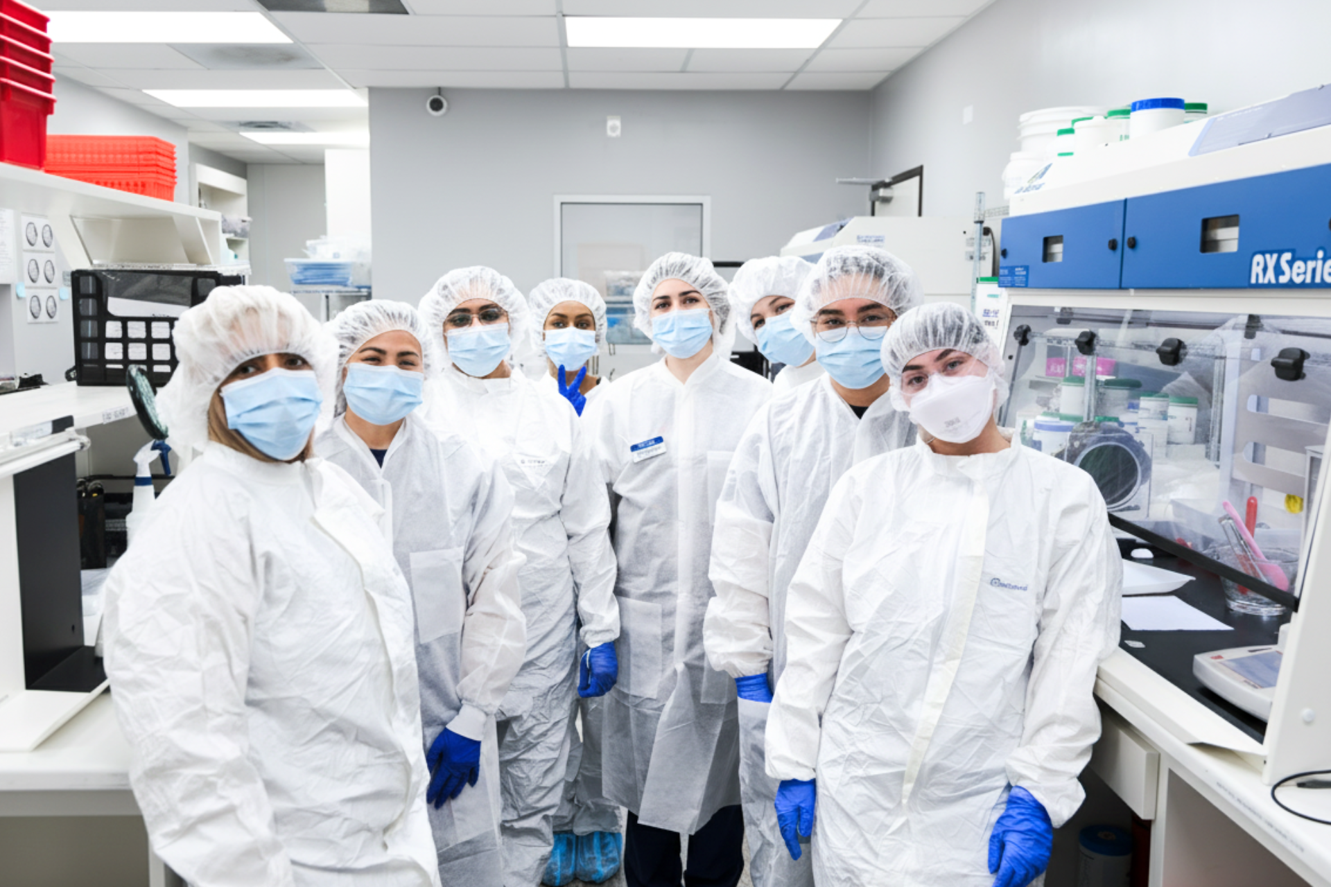 Group of healthcare professionals wearing protective suits, hairnets, masks, and gloves standing in a laboratory.