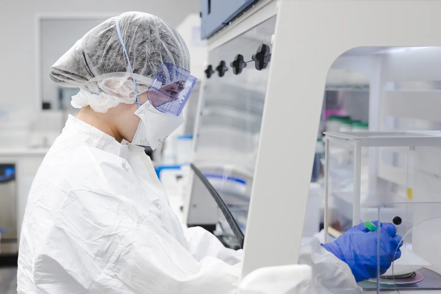 Group of healthcare professionals wearing protective suits, hairnets, masks, and gloves standing in a laboratory.
