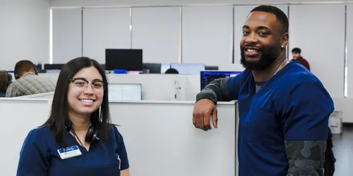 Two healthcare professionals smiling in a modern office with computers and coworkers.