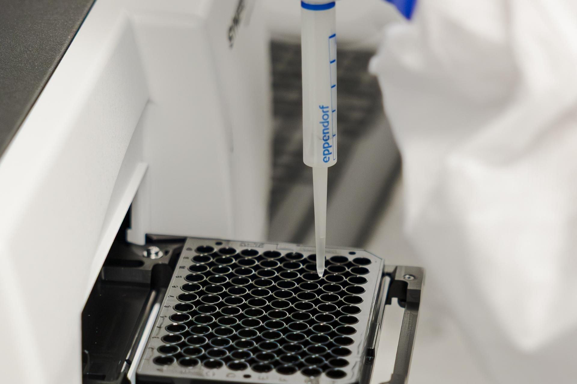 Laboratory technician in protective gear working with samples inside a controlled environment chamber.