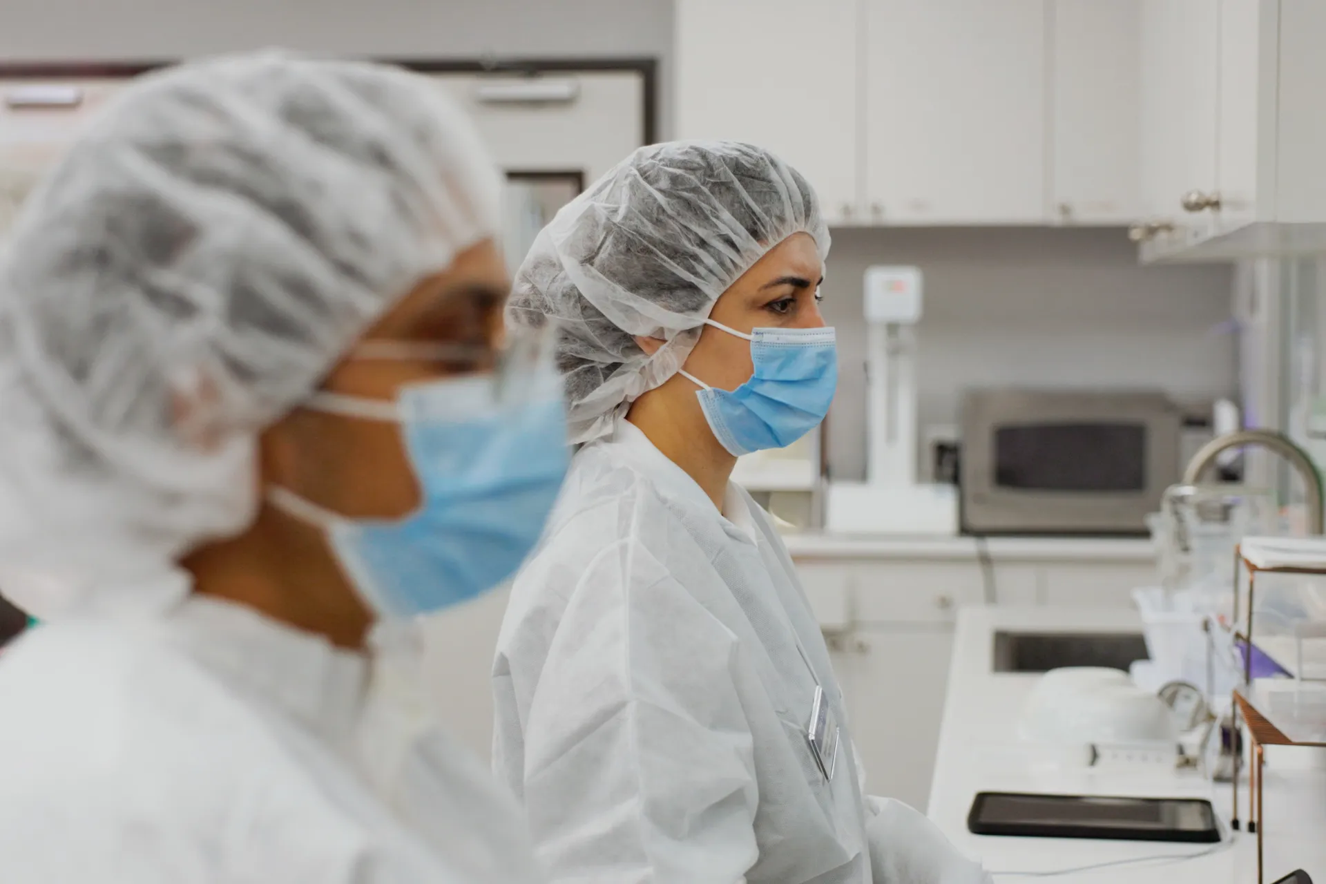 Two healthcare workers wearing masks and hair covers working in a sterile medical laboratory.