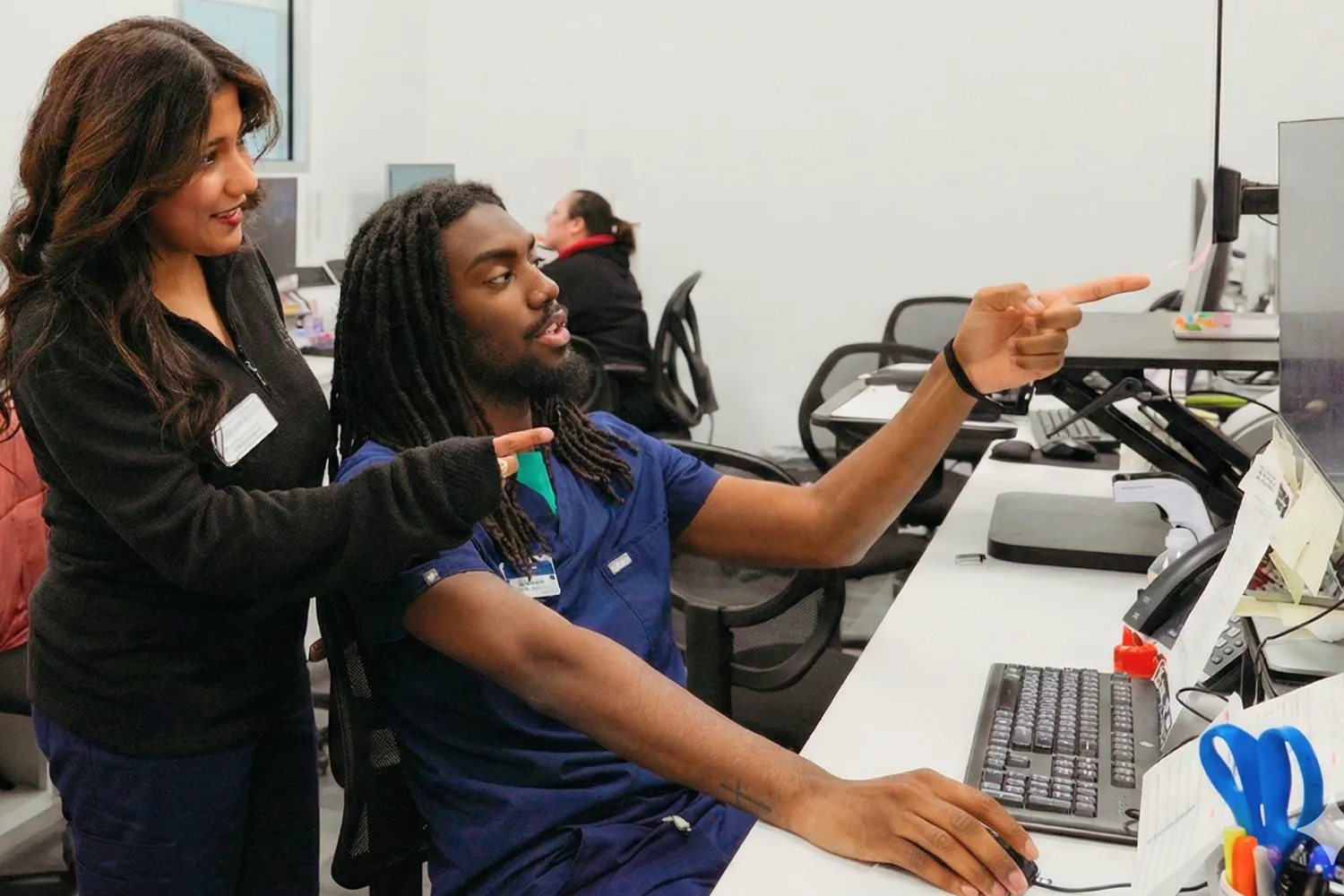 Two medical professionals collaborating while looking at a computer screen in a clinical setting.