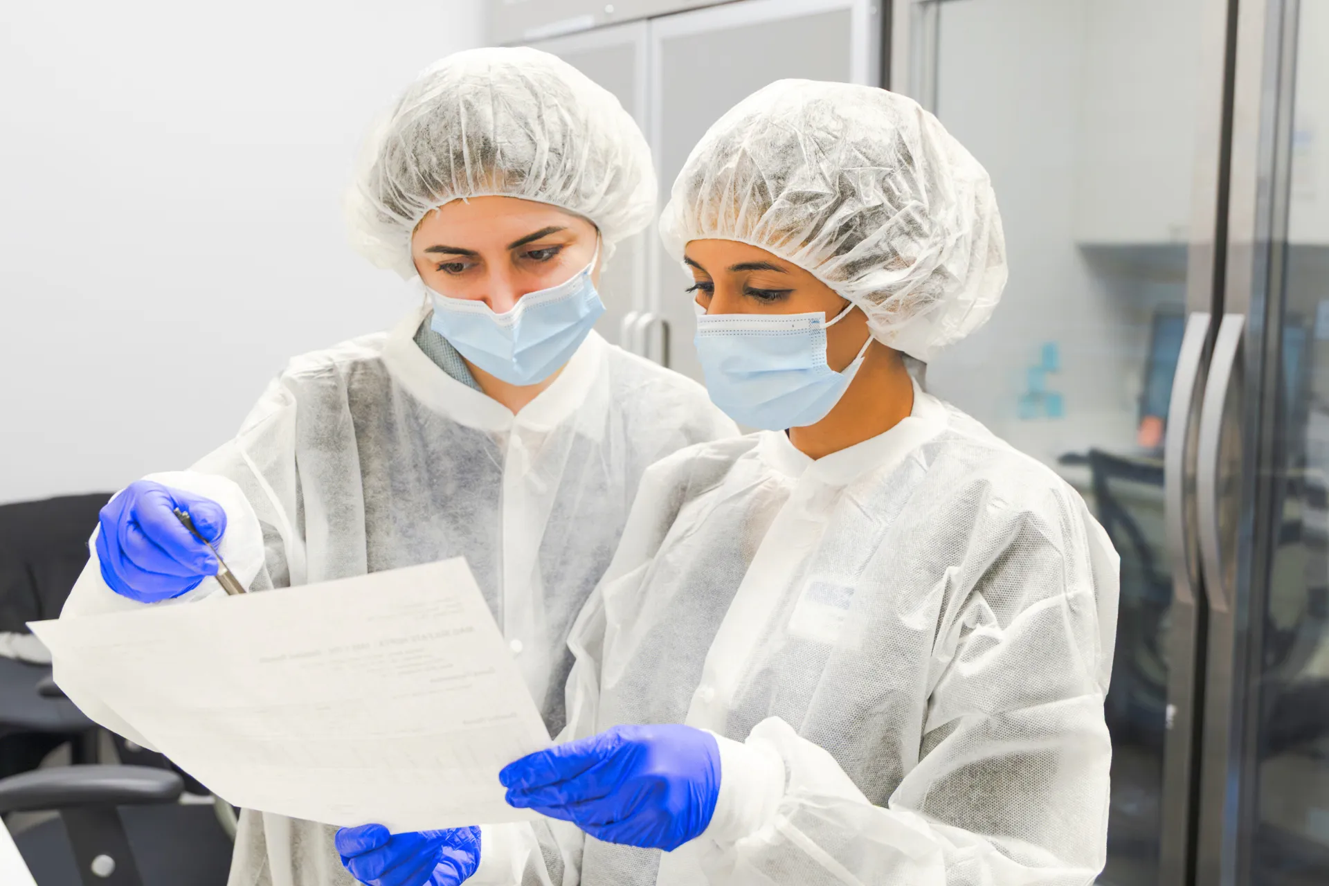 Two women sitting at a table looking at a laptop, one wearing a Thesis Pharmacy uniform.