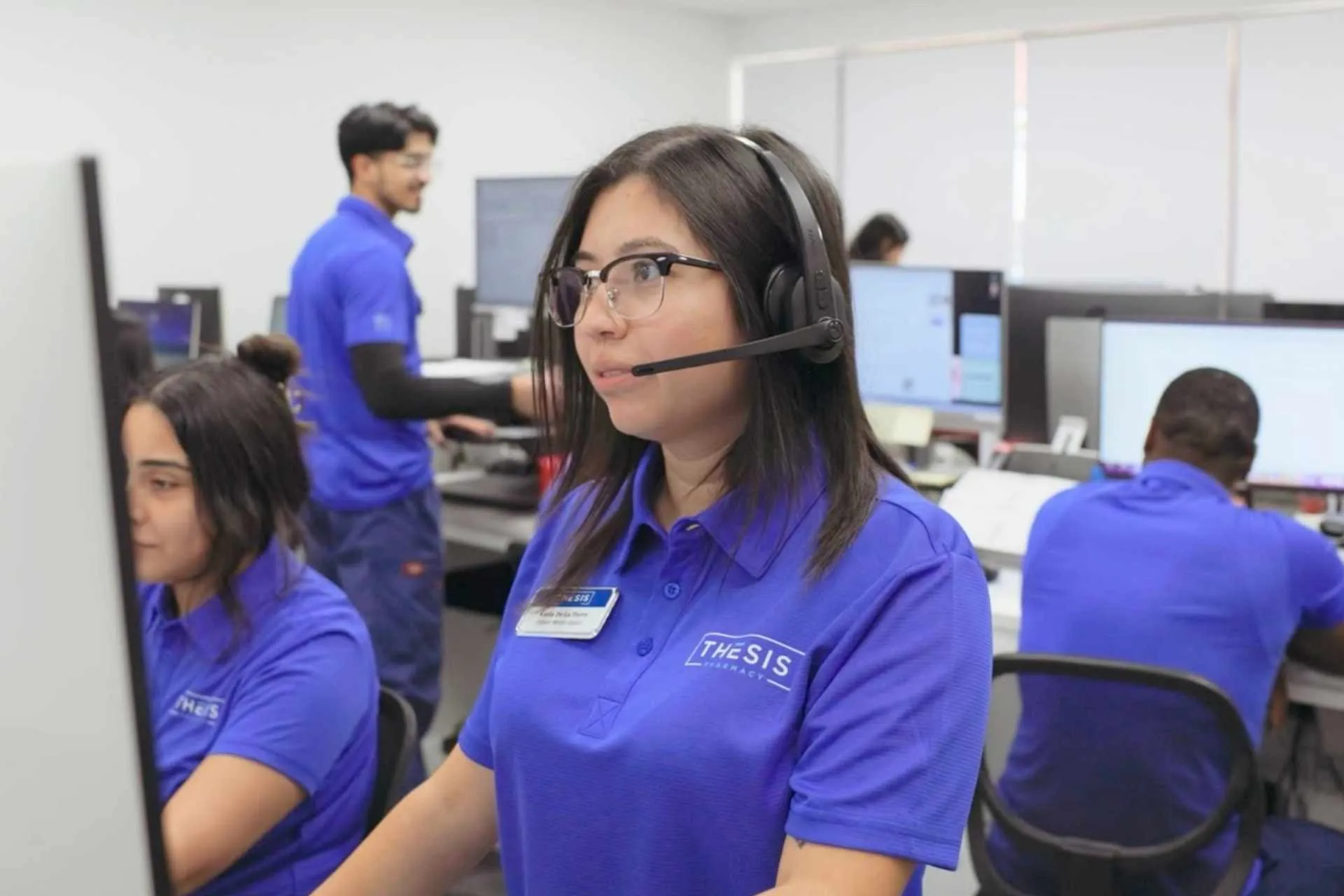 Call center employees in blue shirts working at desks with computers and headsets in a busy office.