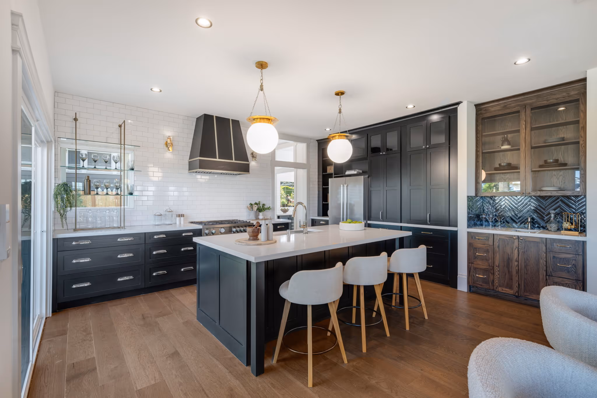 Modern kitchen with black cabinetry, white countertop island, three beige bar stools, and large globe pendant lights.