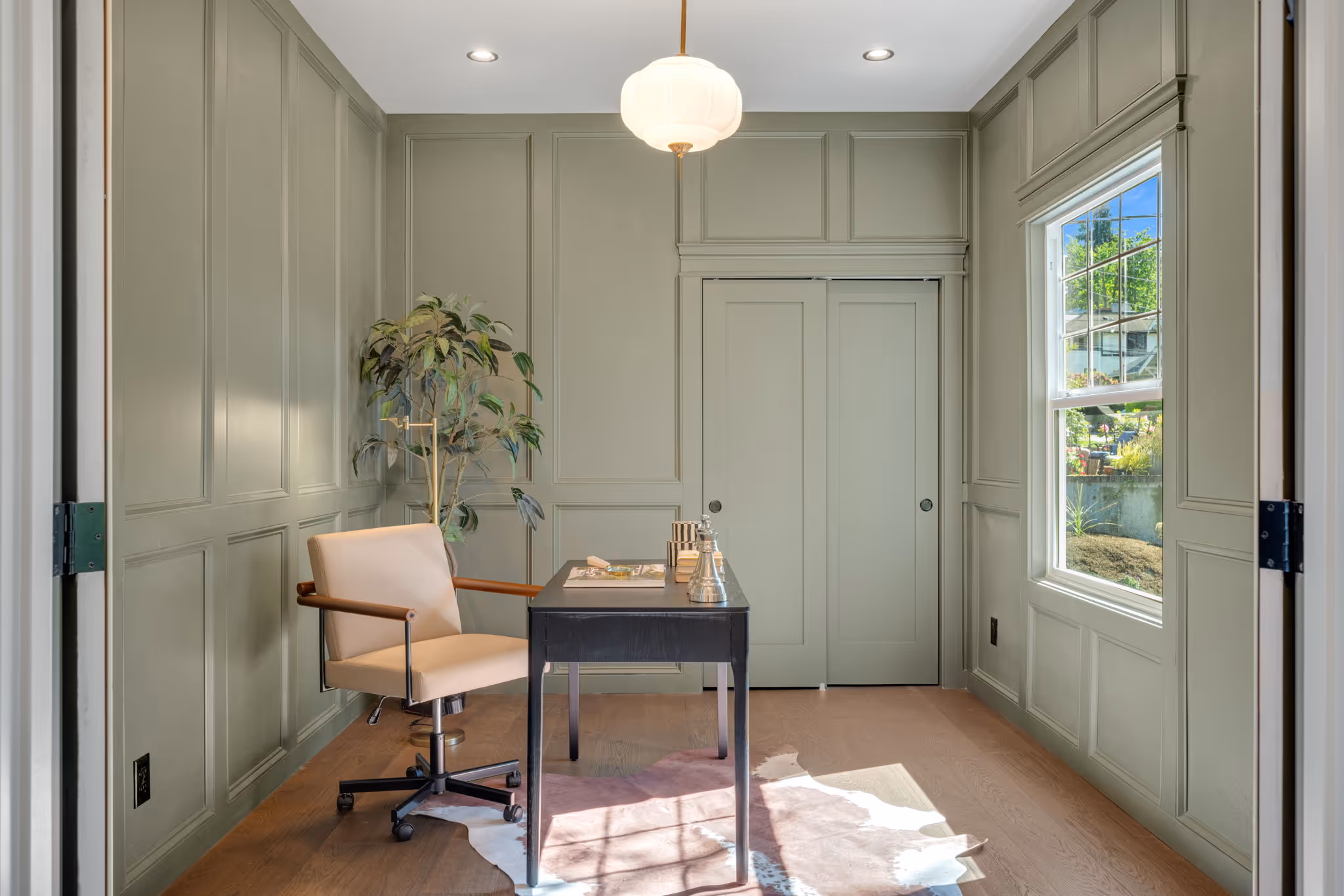 Minimalist home office with a beige chair, black desk, indoor plant, and green paneled walls.