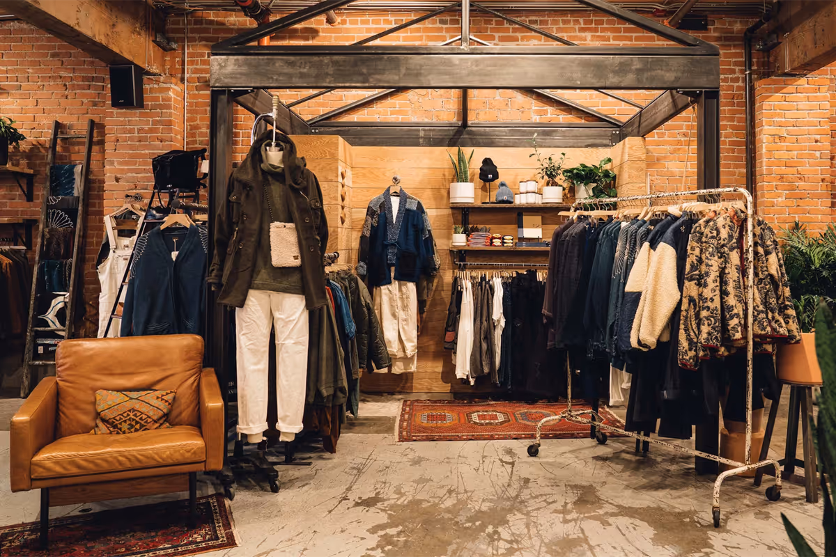 Interior of a boutique clothing store with racks of jackets, sweaters, and a brown leather armchair.