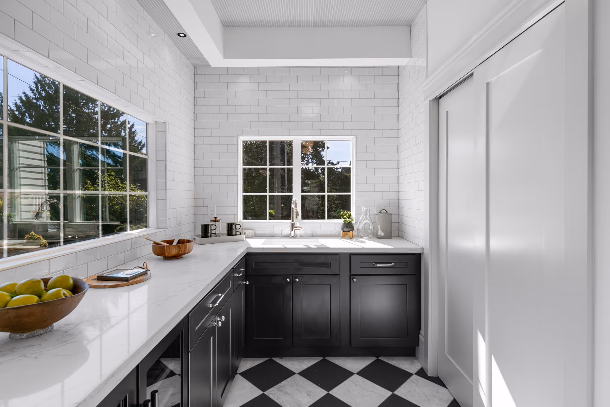 Bright kitchen with white subway tile walls, black cabinets, white countertops, and checkered black and white tile floor.
