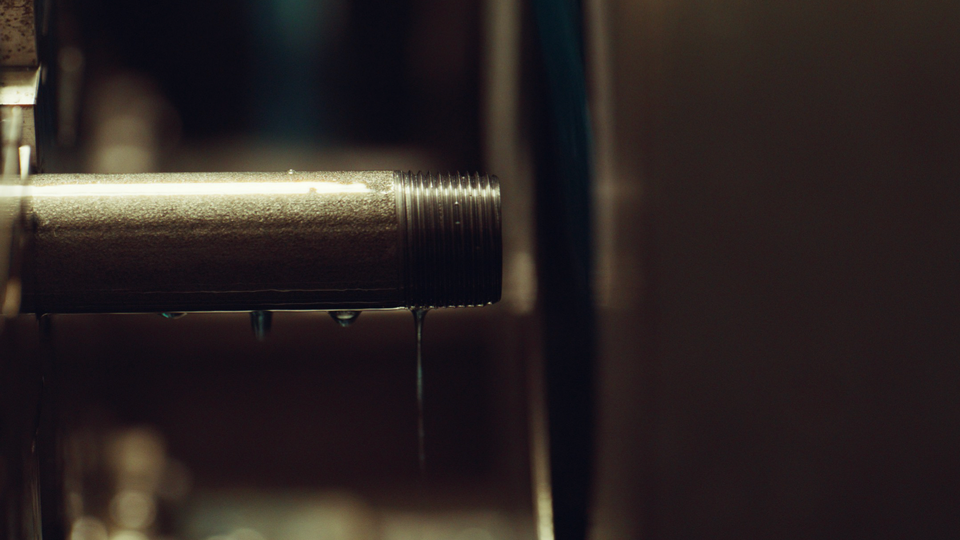 Close-up of a metal pipe with water dripping from its threaded end in a dimly lit setting.