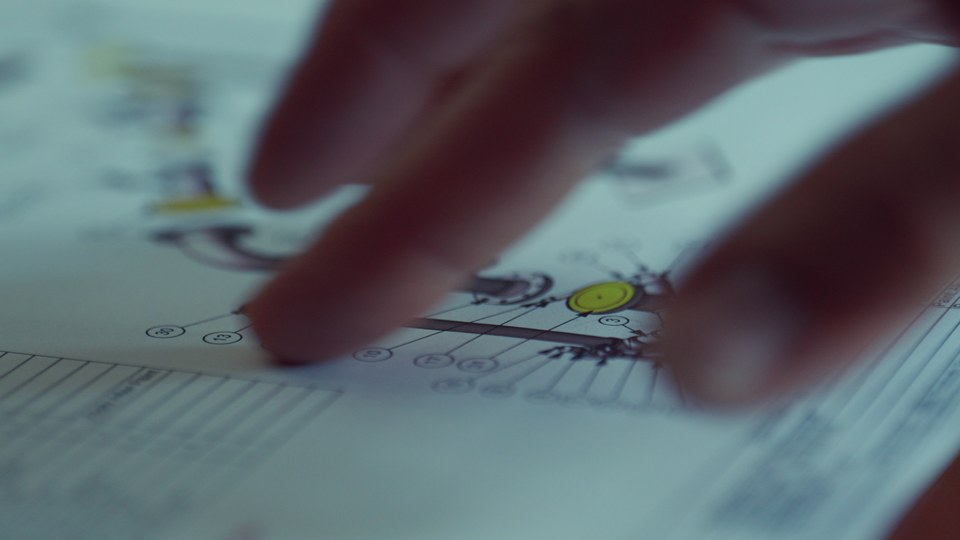 Close-up of fingers pointing at a technical drawing with numbered parts and labels.
