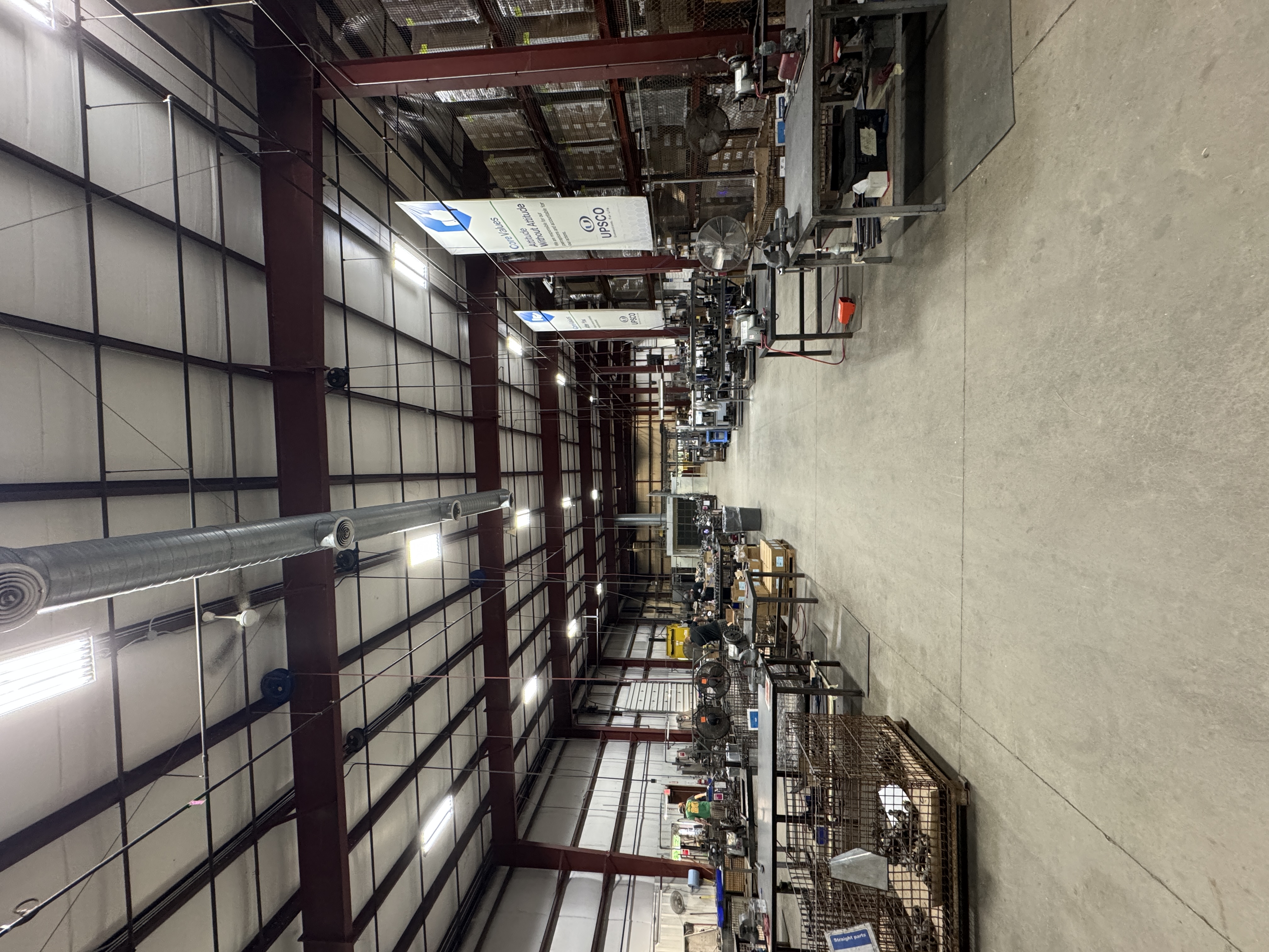 Wide view of a spacious industrial warehouse with metal shelves, work tables, and overhead lighting.