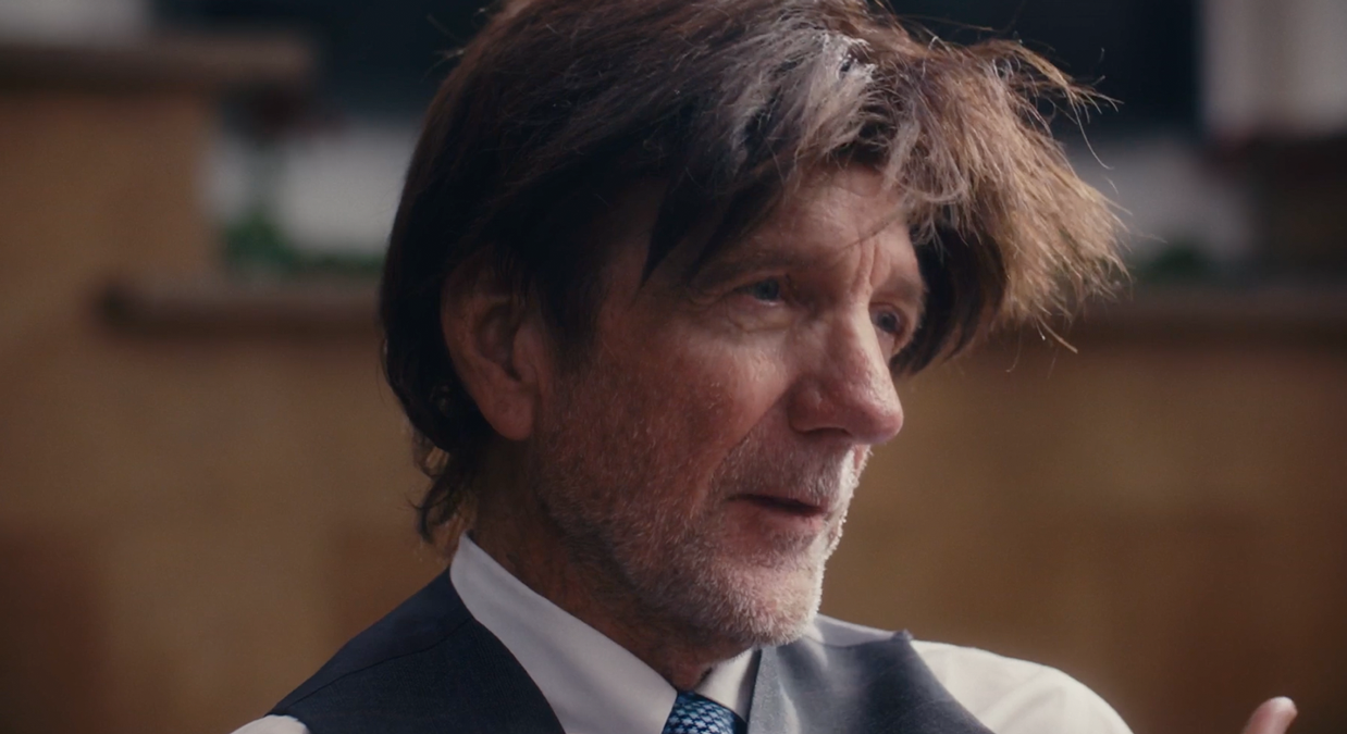 Profile of a middle-aged man with messy hair and beard wearing a shirt, vest, and tie.