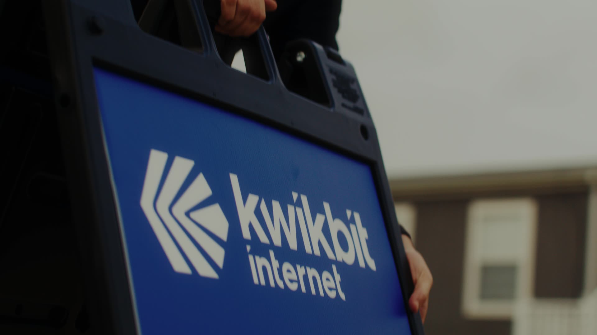 Blue sign with white logo and text reading 'kwikbit internet' held by a person.