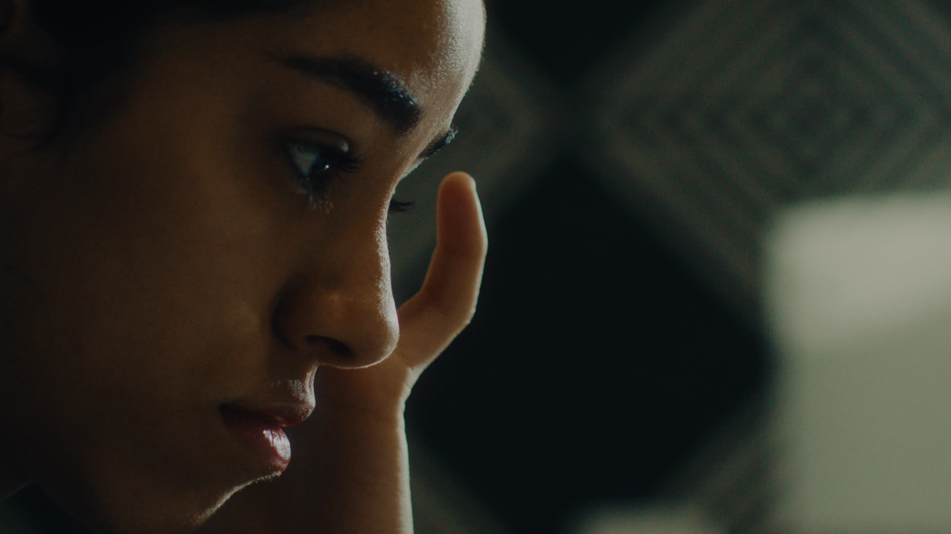 Close-up of a pensive woman resting her face on her hand against a blurred dark background.
