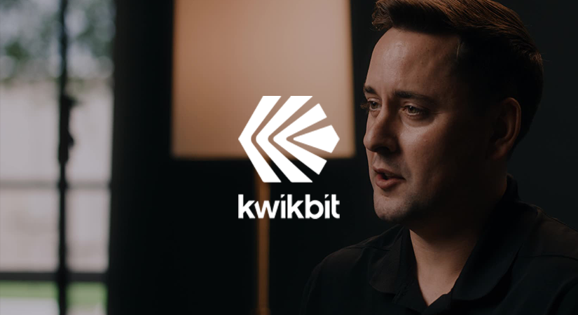 Man in black shirt speaking with a blurred window and lamp in the background and kwikbit logo.