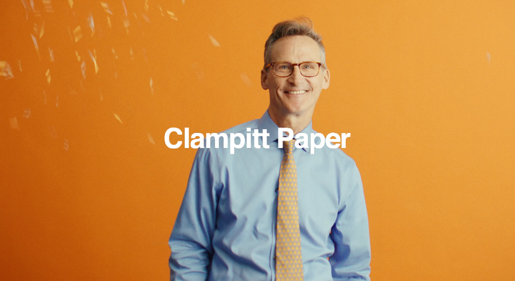 Smiling man with glasses in blue shirt and patterned tie on orange background with text Clampitt Paper.