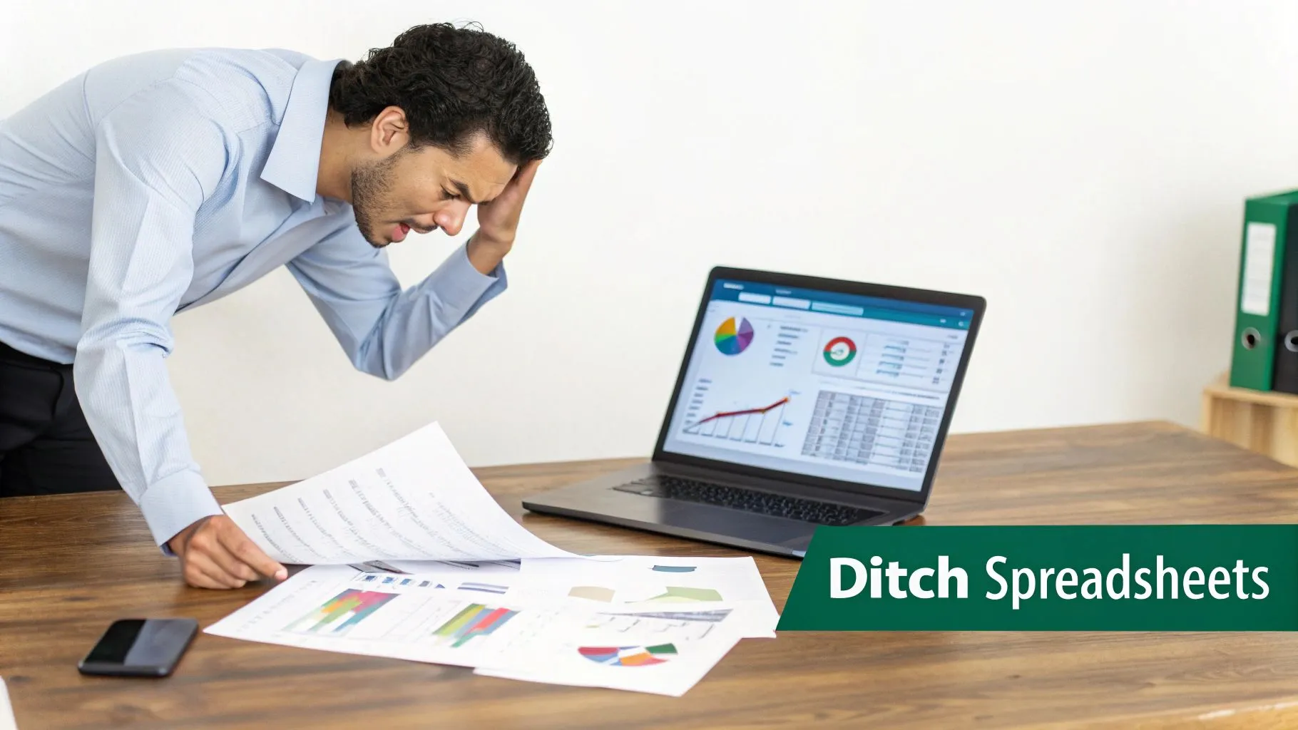 Stressed businessman holding his head, looking at papers with charts and a laptop displaying financial data.