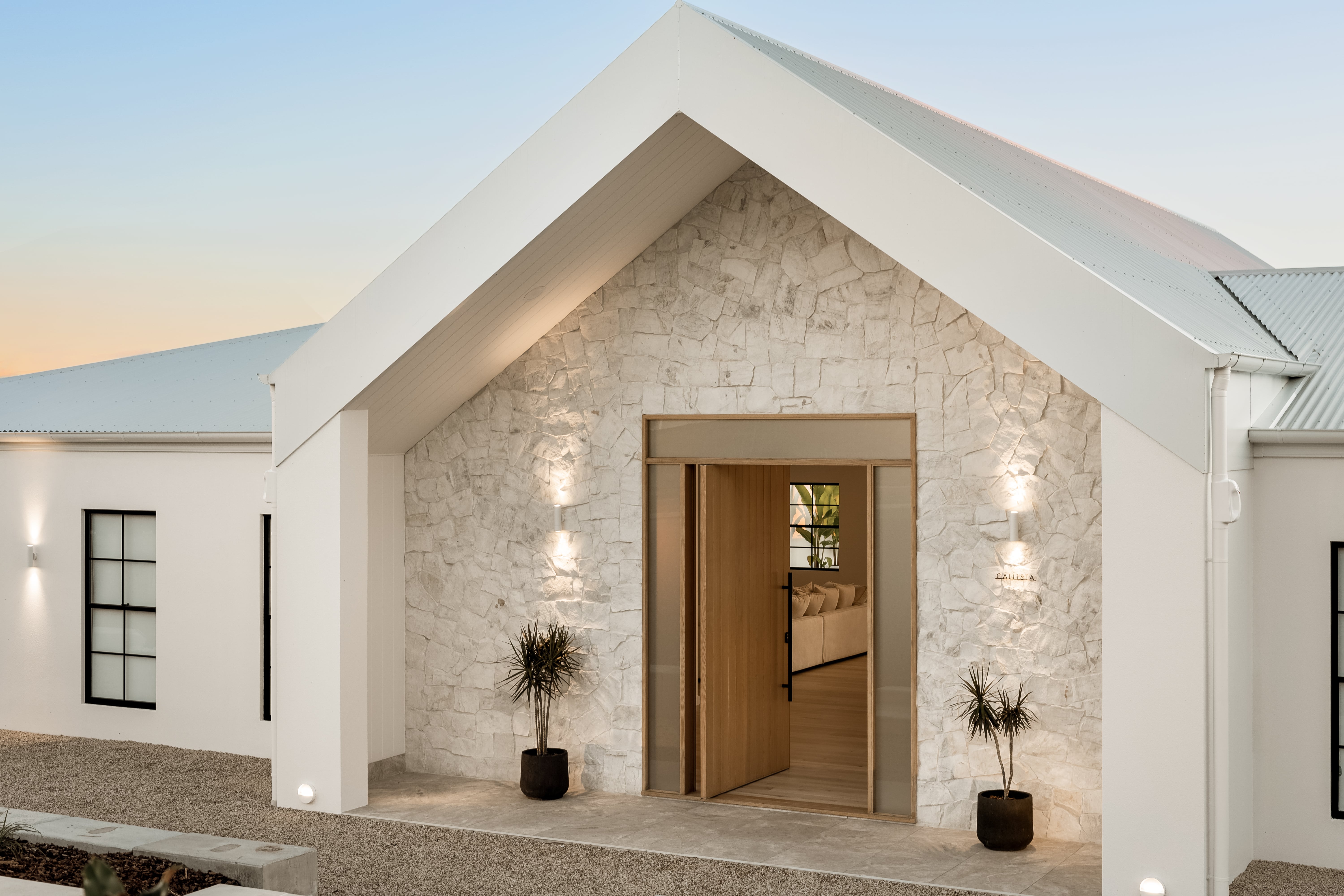 Exterior entrance of Callista by The Renew Company featuring a gabled roof, stone façade, wooden front door, and modern architectural design with warm lighting.