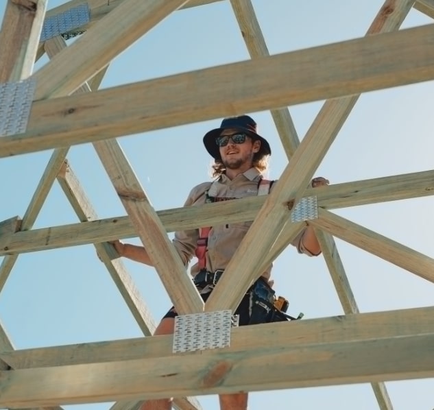 Construction worker securing wooden trusses on house roof frame – The Renew Company eco-friendly home build.