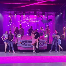 Troupe de danseurs sur scène posant devant une voiture américaine rose lors d'un spectacle sur le thème de Dirty Dancing.