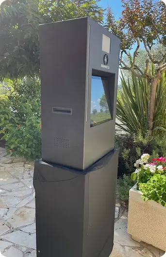 Une borne photobooth verticale de couleur noire, installée en extérieur dans un jardin.