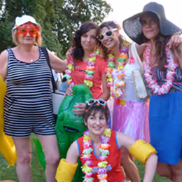 Un groupe de personnes, adultes et un enfant, posant joyeusement en plein air, vêtus de costumes colorés, avec des colliers de fleurs et des jupes.