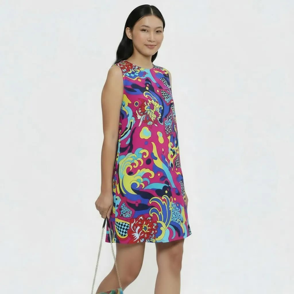 Woman wearing a sleeveless, colorful floral and abstract patterned dress holding a small handbag with a chain strap.