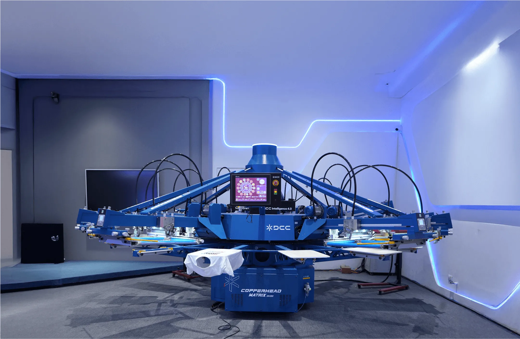 Blue automated screen printing machine with multiple arms and a touchscreen control panel in a modern, lit room.