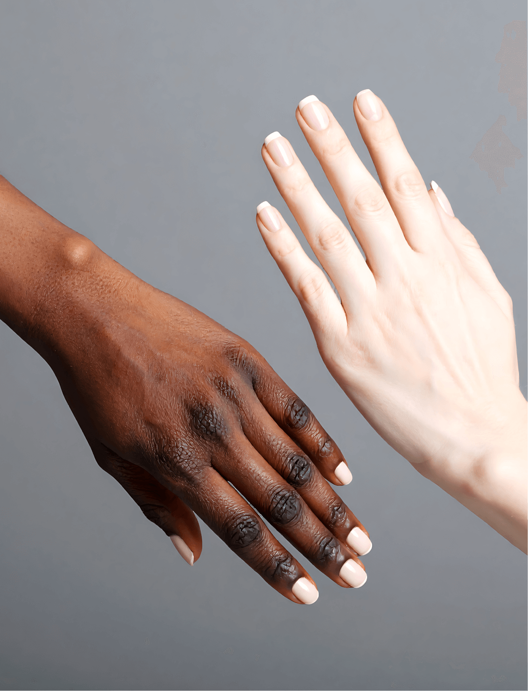 Close-up of two hands, one with dark skin and the other with light skin, both with light pink nail polish, against a gray background.