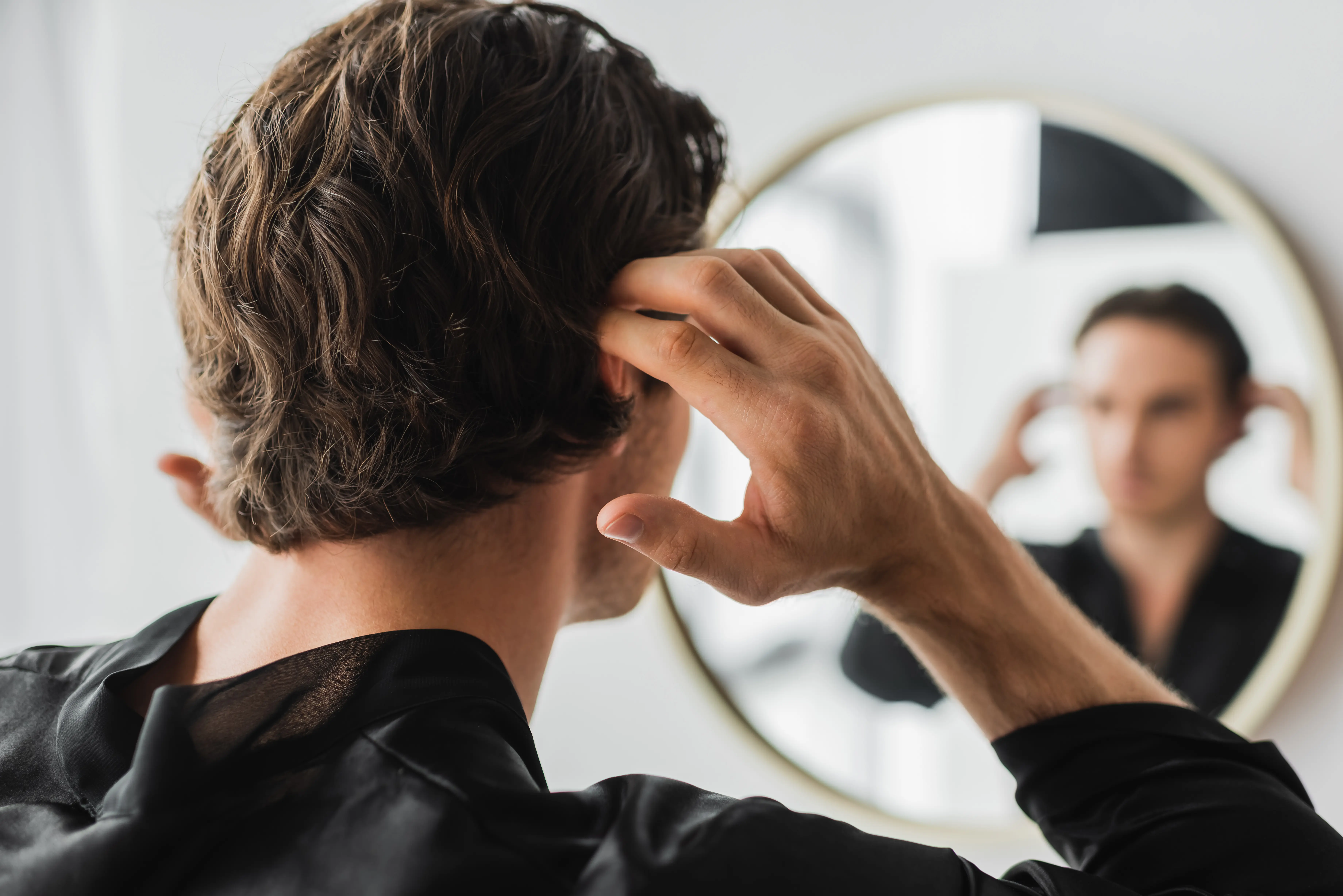 A man combing his hair in front of a mirror.