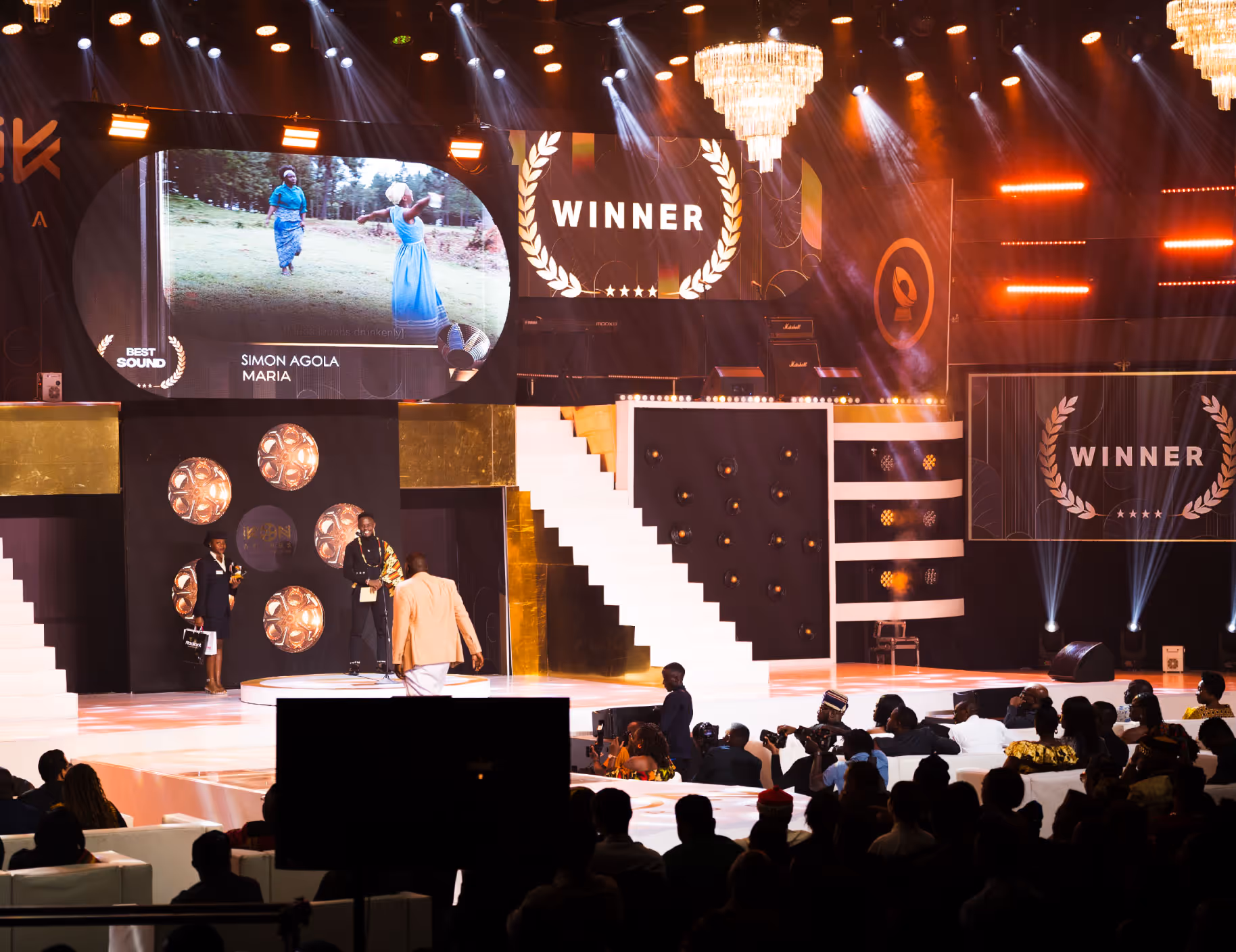 Award ceremony stage with winner announcement and audience watching in formal attire.