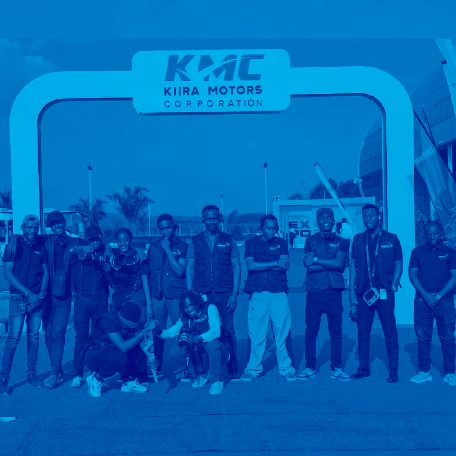 Group of people posing in front of Kiira Motors Corporation archway outdoors.