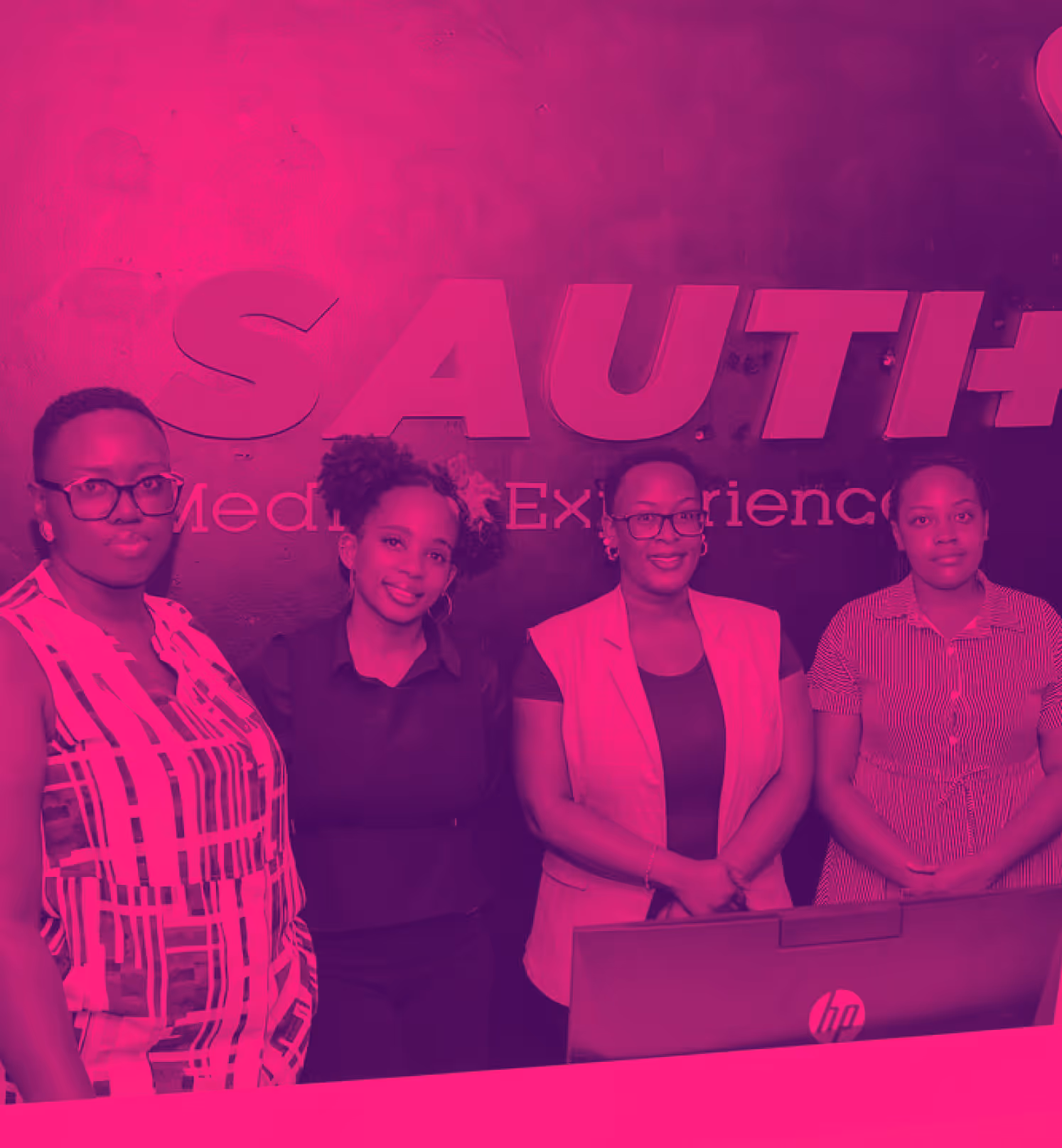 Four women standing behind a reception desk with 'SAUTI' sign in background.
