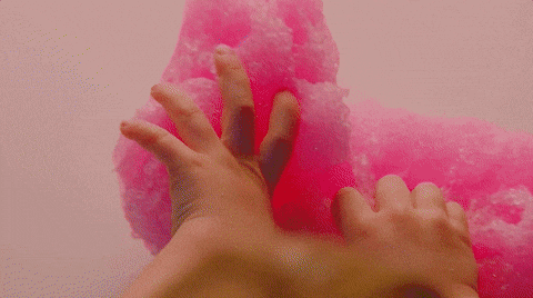 Hands pressing and squeezing pink fluffy cotton candy against a light background.