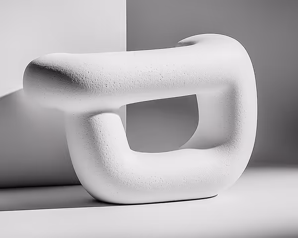 White abstract sculpture with a rough textured surface placed on a light surface against a gray wall.
