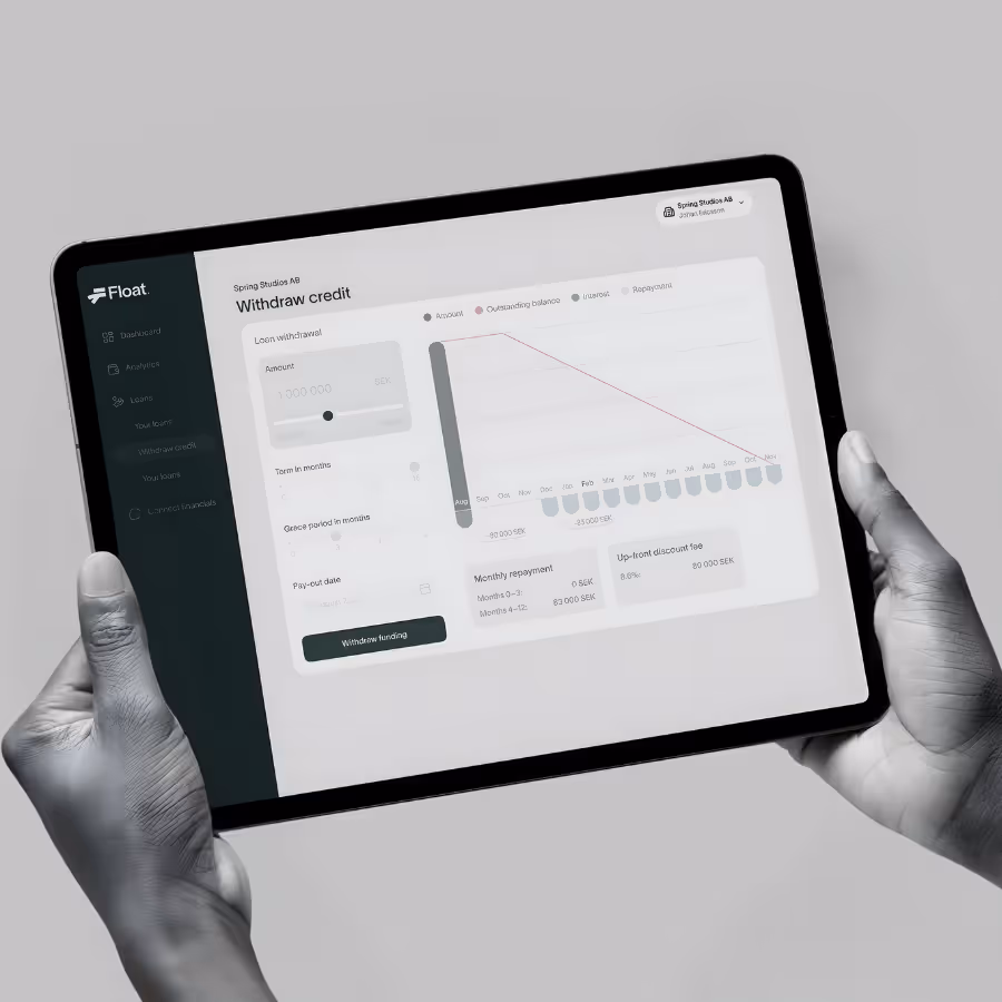 Tablet held by two hands displaying a loan withdrawal credit dashboard from Float with graphs and input fields.
