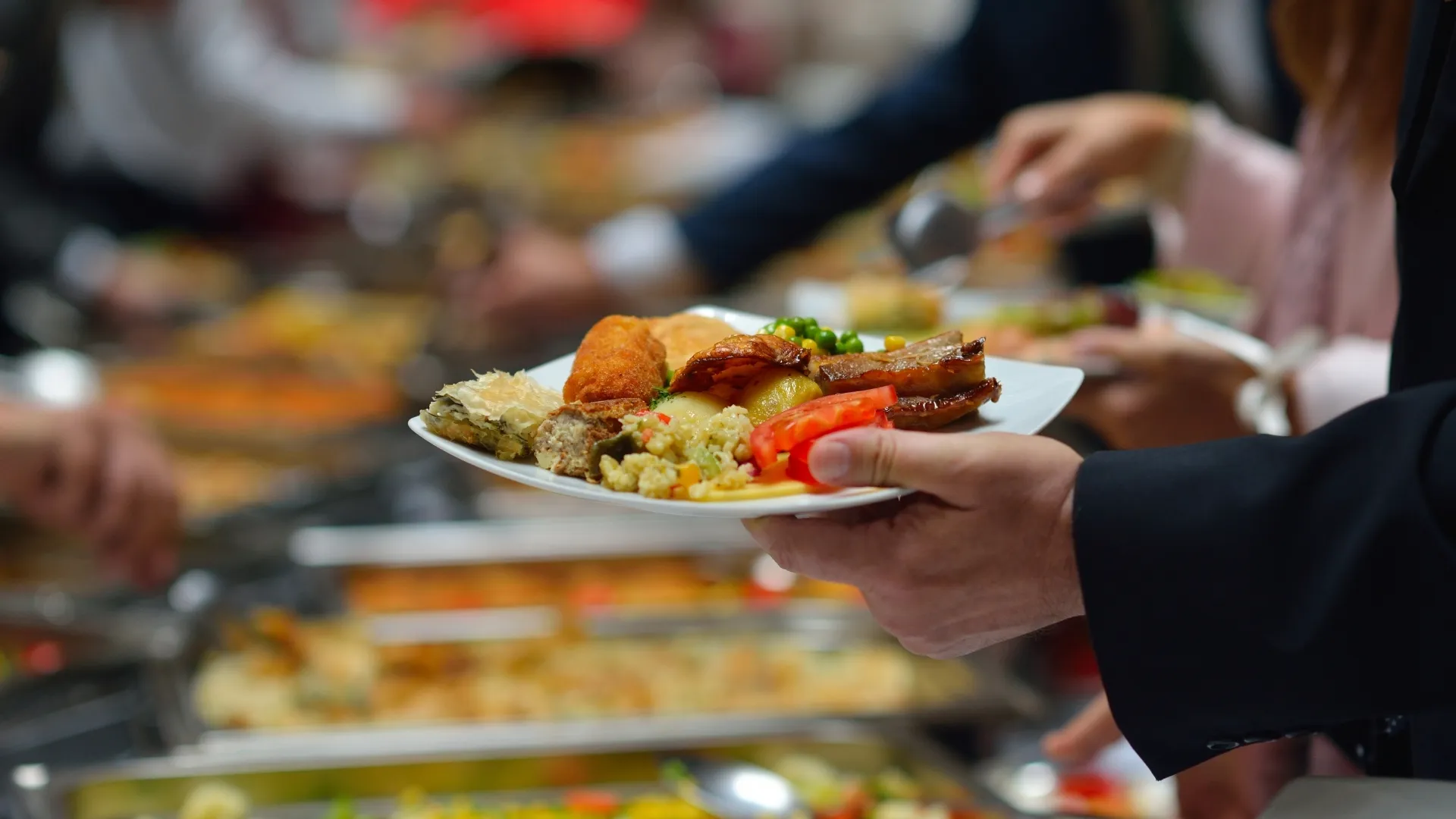 A hotel guest using silver tongs to plate food at a luxury breakfast buffet line, representing mindful consumption in sustainable tourism. 