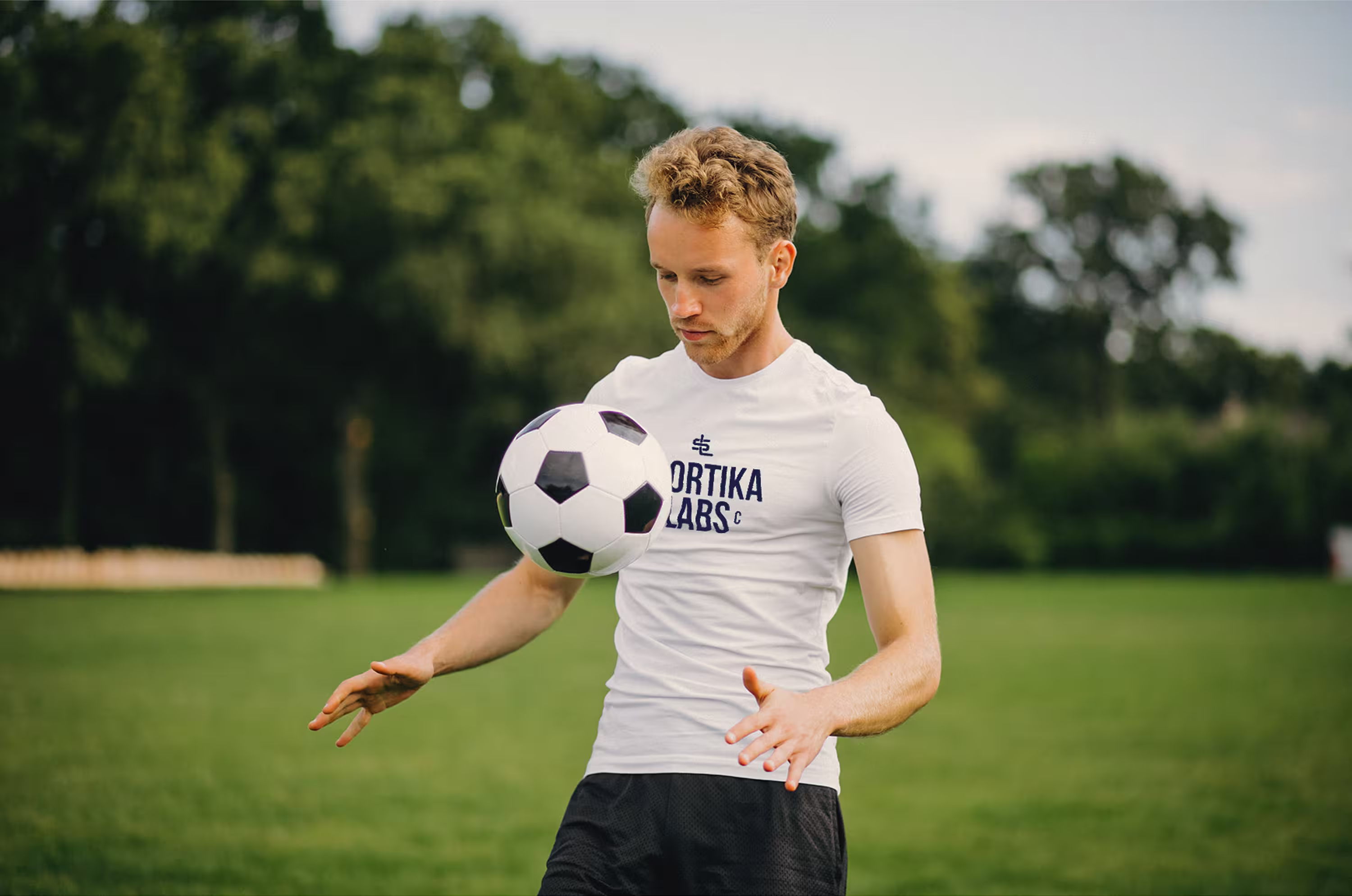 Young man juggling a soccer ball on the field wearing a Sportika Labs T-shirt.