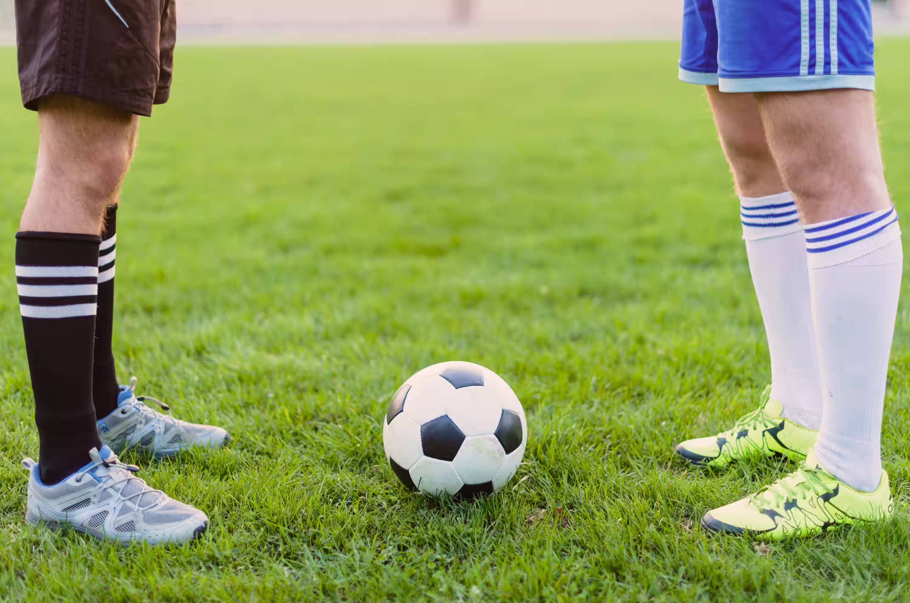 Two soccer players standing face to face with a ball between their feet on the grass field.
