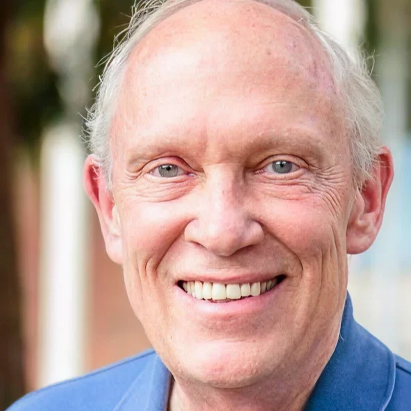 Smiling older man in a blue polo shirt poses outdoors in natural light.