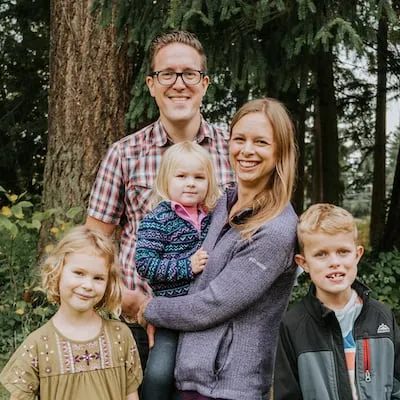 Smiling family of five outdoors with trees in the background, parents and three young children posing together.