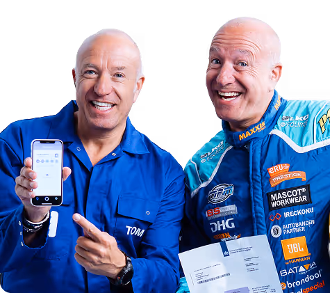 Two smiling men, one in a blue shirt pointing to a smartphone and the other in a racing suit holding papers.