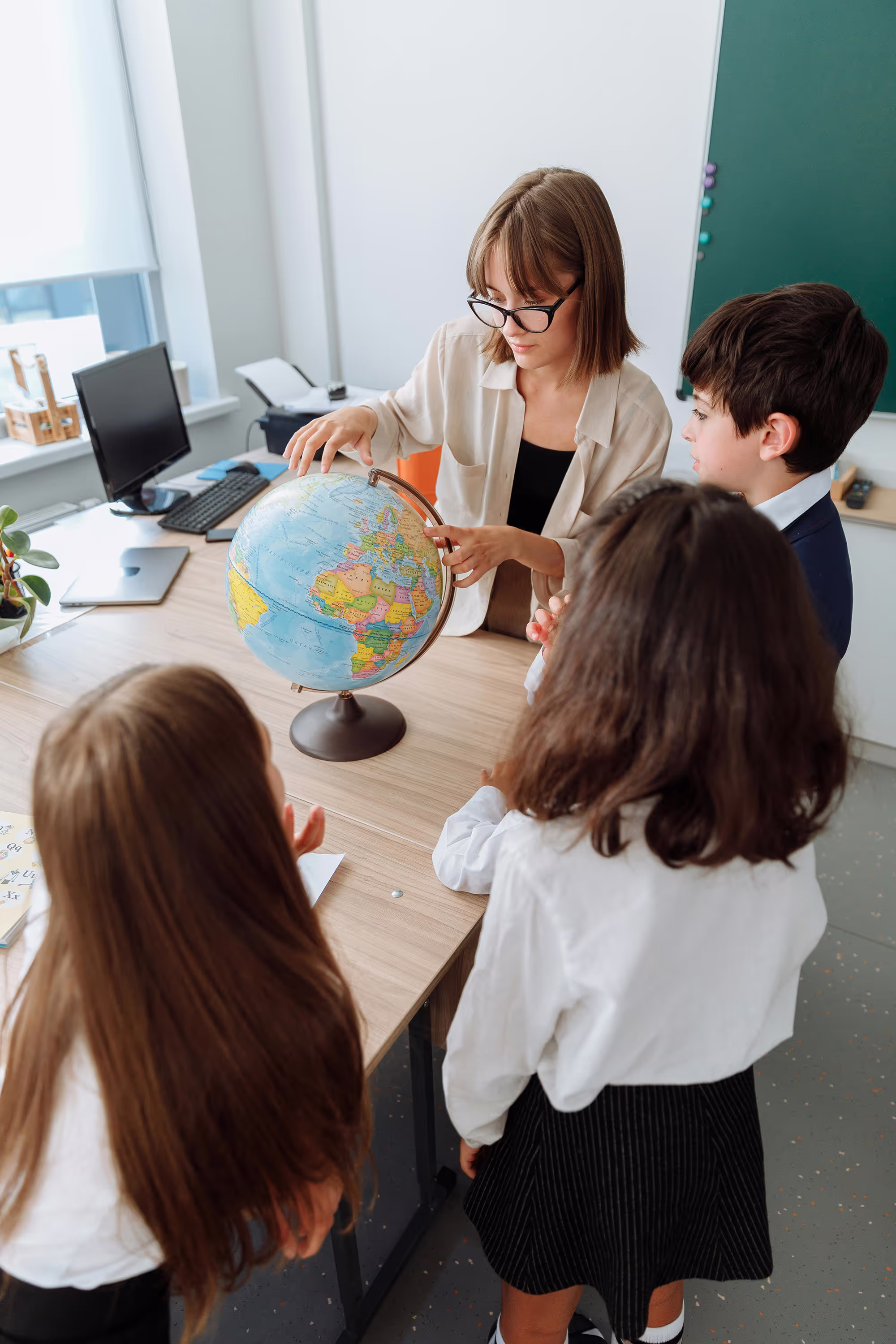 A teacher is showing a globe to a group of students, pointing to different locations as the students watch attentively