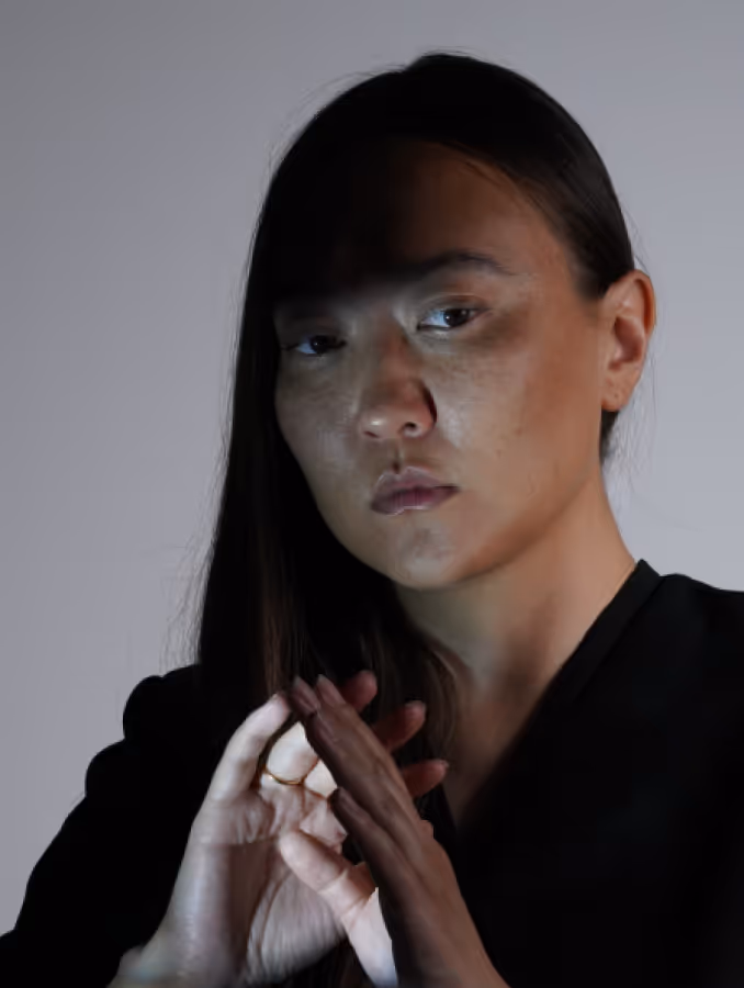 Portrait of a woman with long dark hair wearing a black shirt and holding her chin thoughtfully
