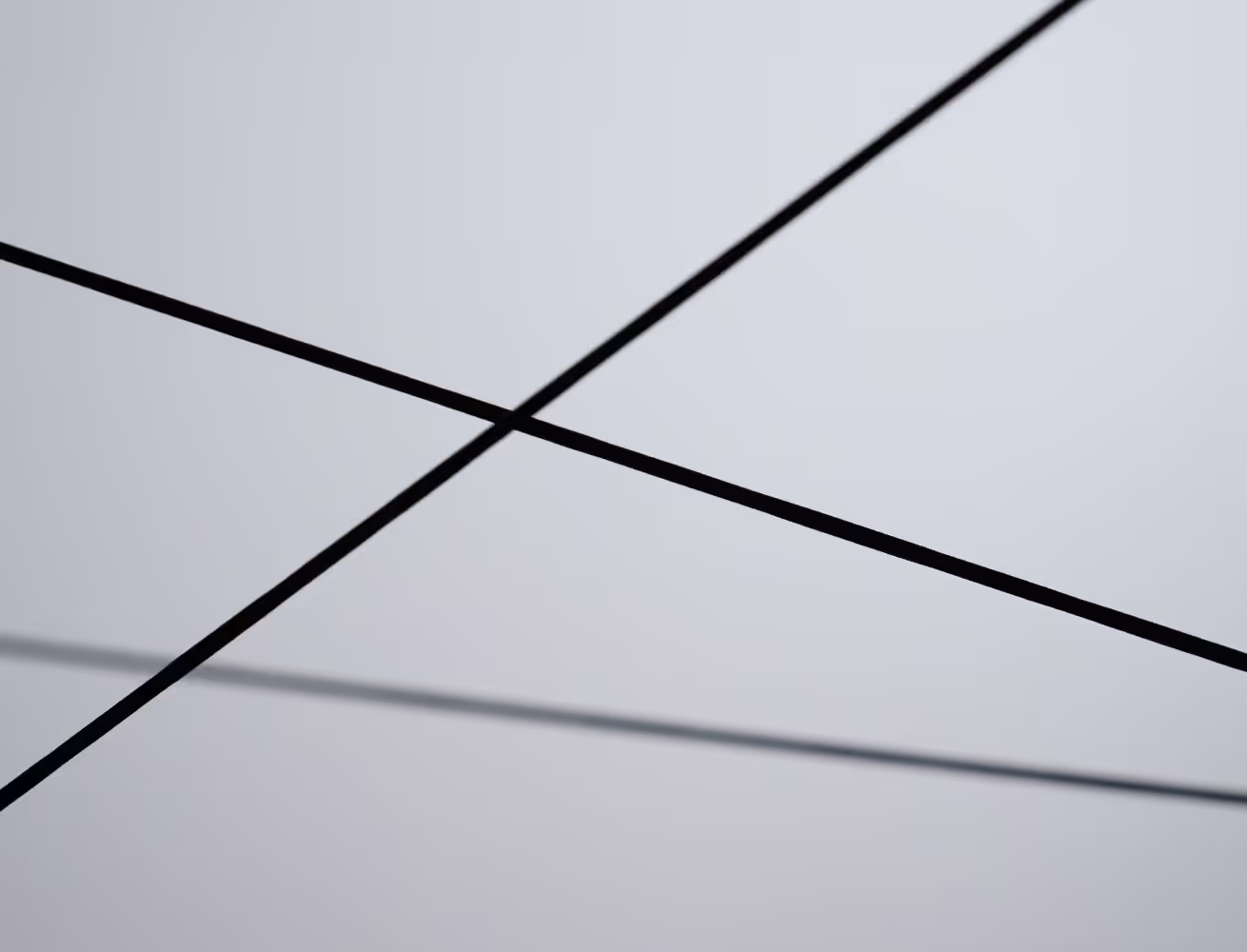 Two intersecting black power lines against a plain gray sky.