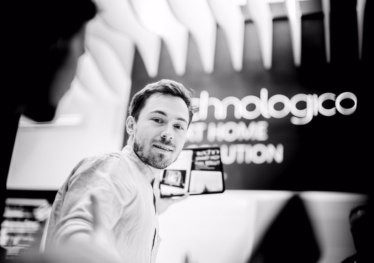 Man holding a tablet and smiling, with blurred text 'Technology at Home Solution' in the background.