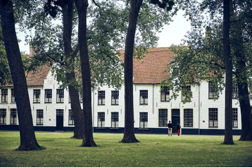 Langgestrecktes weißes Gebäude mit rotem Ziegeldach in parkähnlicher Umgebung mit altem Baumbestand