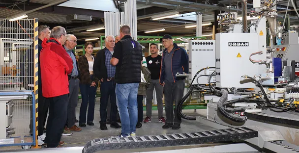 Groupe de personnes en visite guidée dans l'atelier Domofen SA de Courgenay avec des machines industrielles visibles.