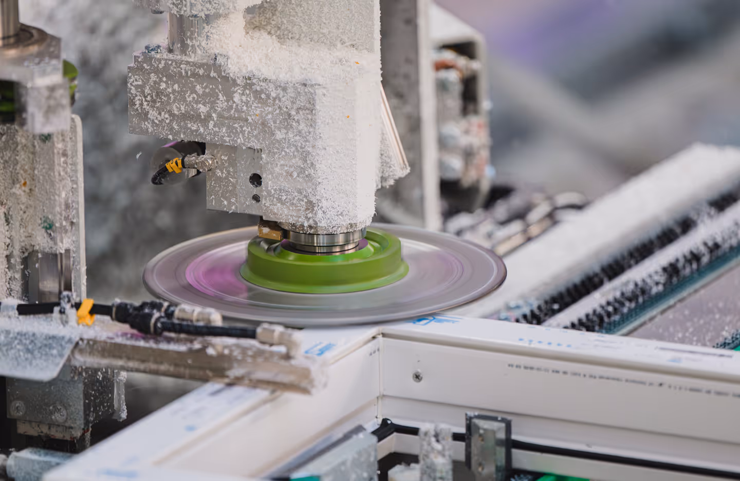 Machine industrielle en train de fraiser une pièce avec un disque rotatif vert et des copeaux blancs autour.